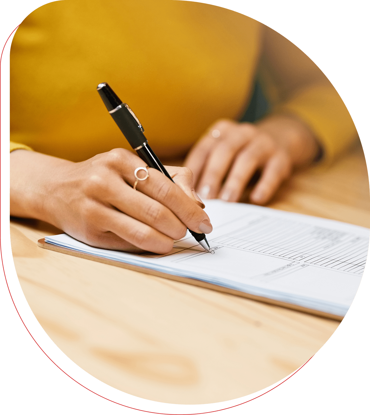 Person writing in a notebook with a pen on a wooden table.